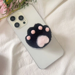 Close-up of a cute black plush cat paw phone grip with pink felt pads on a white smartphone