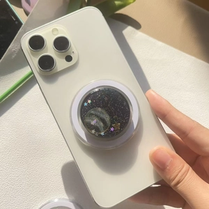 Nahaufnahme eines Handy-Griffs im Planeten-Design mit Glitzersternen auf einem Smartphone
