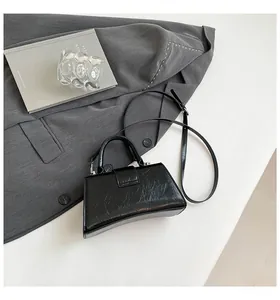 Detail of black glossy hourglass bag with crinkle texture on a grey blazer background