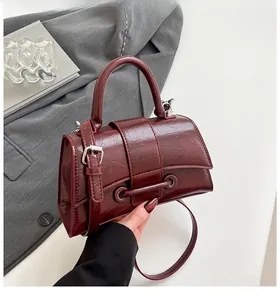 Detail of burgundy glossy embossed leather handbag with metal bar and sleek handle