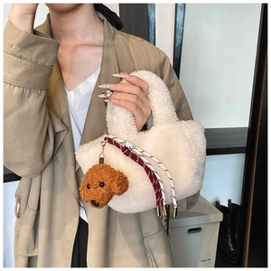 Close-up of white plush bucket bag with brown teddy dog charm and woven strap details