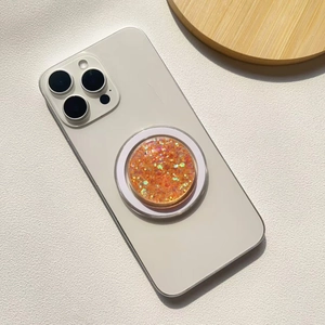 Detailed close-up of a sparkling orange glitter phone grip on a white smartphone case