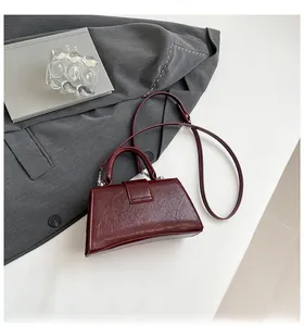 Detail of burgundy hourglass bag with pleated texture and adjustable strap on a white table