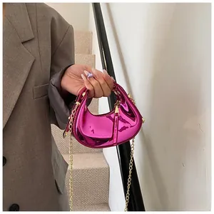 Detail of fuchsia patent leather crescent mini bag with gold chain strap held by model