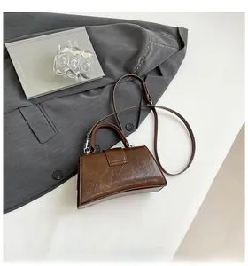 Detail of dark brown hourglass handbag with glossy wrinkled texture on a grey background