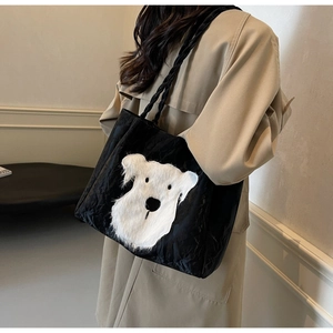 Detail view of black tote bag with 3D plush puppy patch on model in beige coat