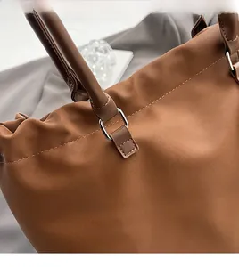 Detailed close-up of dark brown tote bag with silver metal buckle and stitching