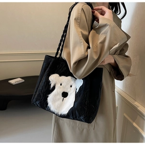 Detail of a black tote bag featuring a plush white dog graphic and woven rope straps
