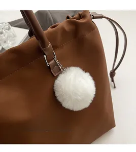Detail of caramel brown leather tote bag with stylish white faux fur ball keychain