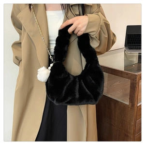 Detail of black faux fur dumpling bag featuring a plush pompom and pearl chain