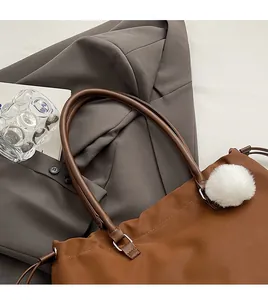 Close-up of brown tote bag with leather handles and white plush charm on office attire