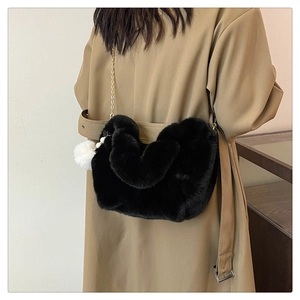 Detail of black faux fur dumpling bag with gold chain strap and plush pompom charm