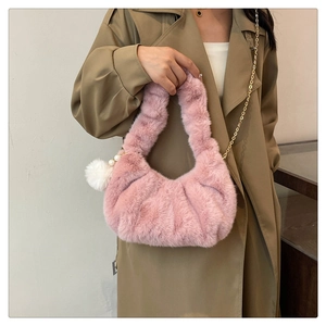 Detail of pink faux fur dumpling bag featuring gold chain and white fluffy ball pendant