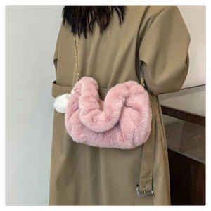 Detail of pink faux fur crossbody bag with gold chain and pearl charm on a model