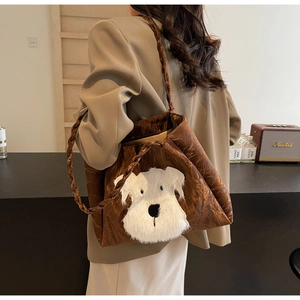 Close-up of brown pleated tote bag with a white plush puppy patch and woven strap