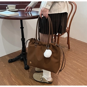 Detail of caramel tote bag with drawstring closure and white pompom charm in lifestyle setting