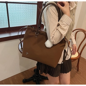 Detail of a deep brown tote bag with drawstring design and white plush charm on wood