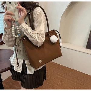 Detail of a brown large capacity tote bag with drawstring closure and plush ball charm