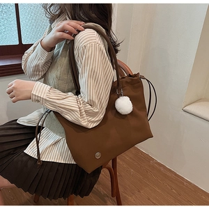 Detail of brown tote bag with side drawstring and fluffy white pompom charm