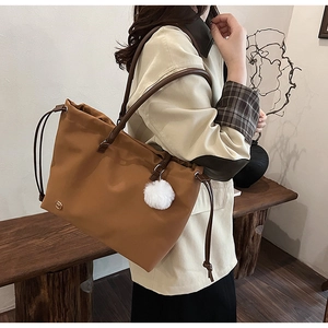 Detail of earthy brown tote bag featuring drawstring closure and white pompom charm