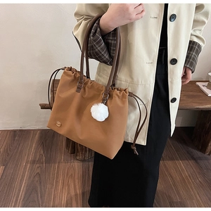 Detailed side view of a large brown tote bag with leather handles and white pom-pom charm