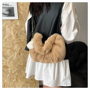 Detail of camel plush dumpling bag featuring golden chain strap and fluffy white pompom