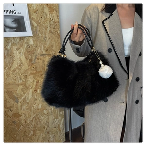 Detail of a black faux fur handbag featuring a fluffy texture and a white pompom charm