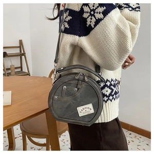 Detail of round grey crossbody bag with denim pocket design and metal studs on the side