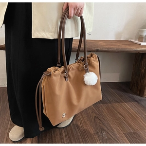 Detail of caramel nylon tote bag with drawstring closure and soft white pompom charm