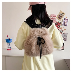 Detail of a brown plush backpack with a black drawstring bow, worn by a female model