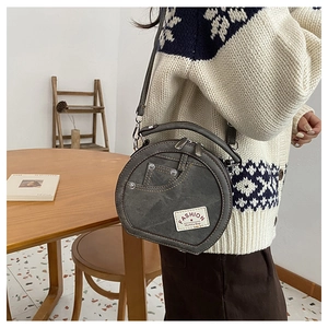 Close-up of circular grey crossbody bag featuring denim-style stitching and rivet details