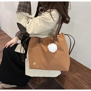 Detail view of a large brown tote bag with side drawstrings and a white pompom charm