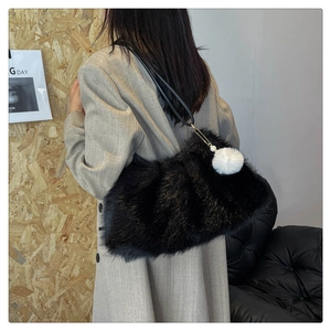 Close-up of black faux fur shoulder bag with white pom-pom and pearl detail on a model