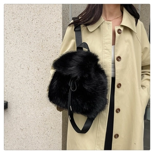 Detail view of a black faux fur backpack with nylon straps shown on a beige trench coat