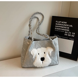 Detail of silver tote bag with braided handles and plush dog embroidery on marble surface