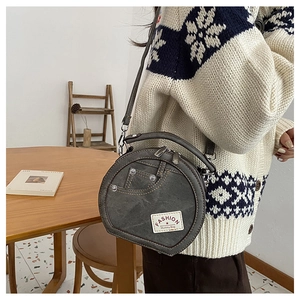 Detail of round grey crossbody bag with white fashion label and contrast stitching texture