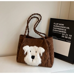 Detail of brown pleated tote bag featuring a plush white puppy patch and woven rope handle