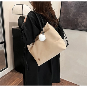 Detail of beige large capacity tote bag with drawstring closure and plush ball charm