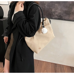 Detail view of a beige crossbody tote with drawstring closure and plush ball charm