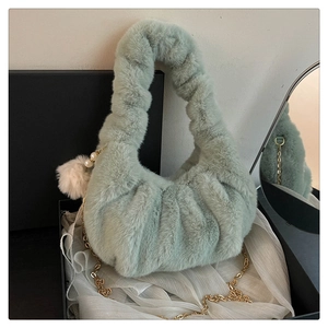 Detail of mint green plush dumpling bag with gold chain and pearl charm on gift box