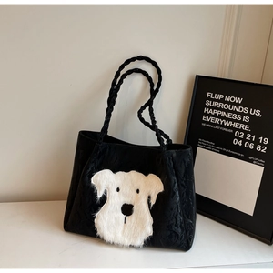 Detail of a black tote bag featuring a 3D plush white puppy patch and woven rope handle