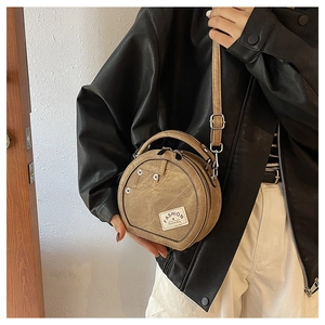 Detail of round camel leather bag featuring retro denim pocket design and metal rivets