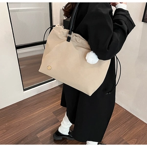 Close-up of minimalist beige canvas tote bag with black strap and plush ball charm