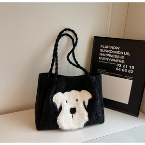 Detail view of large black tote bag featuring a cute white plush puppy patch and braided handle