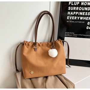 Detail of camel tote bag with drawstring, white fluffy ball charm, and gold metal logo