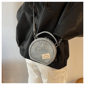 Model wearing a light blue denim round handbag with rivet details and crossbody strap