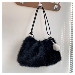 Detail of a fluffy black faux fur shoulder bag featuring a pearl-accented white pompom charm