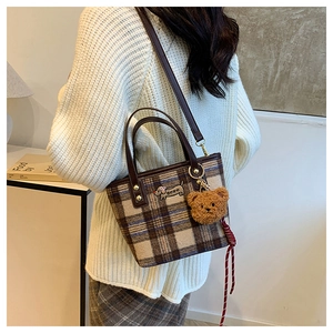 Detail of checkered plaid shoulder bag featuring a cute plush bear charm and puppy patch