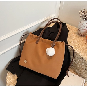 Detail of a brown nylon tote bag with leather straps, drawstring design, and pom-pom charm