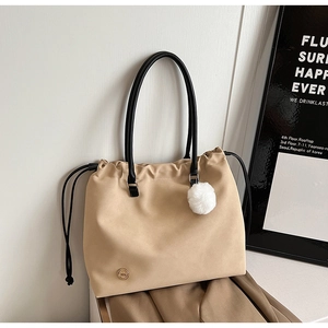 Detail of beige drawstring tote bag with black leather straps and white pompom charm